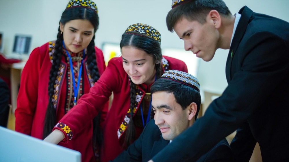 Four young people gather around a computer.