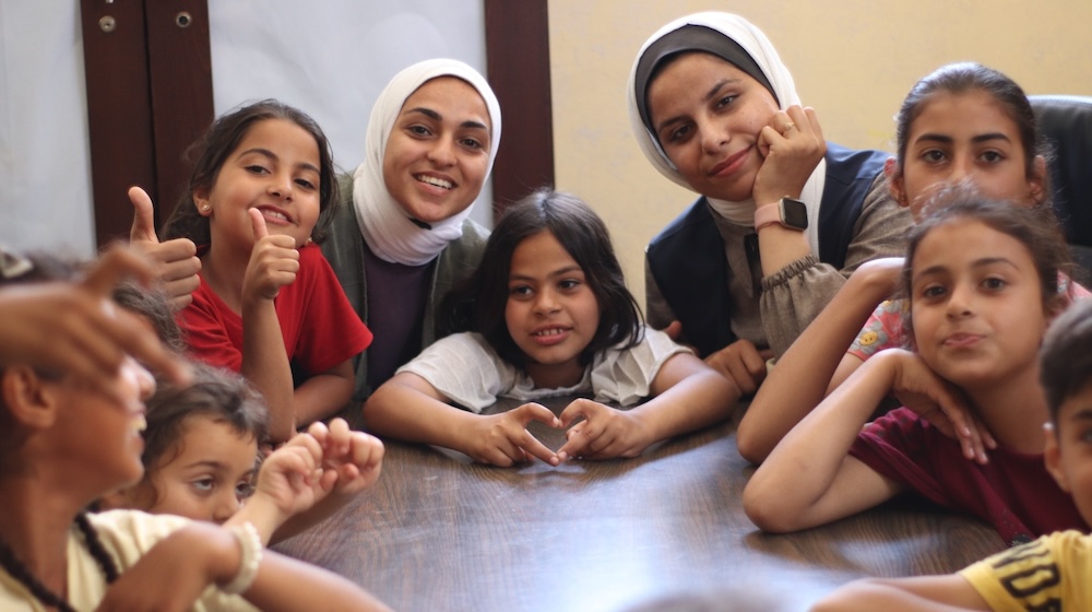 Deux femmes adultes sont assises avec un groupe de jeunes enfants autour d’une table