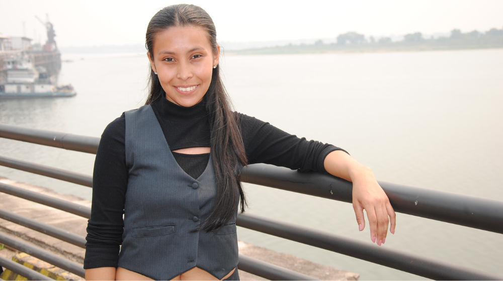 Une jeune femme pose debout devant une étendue d’eau