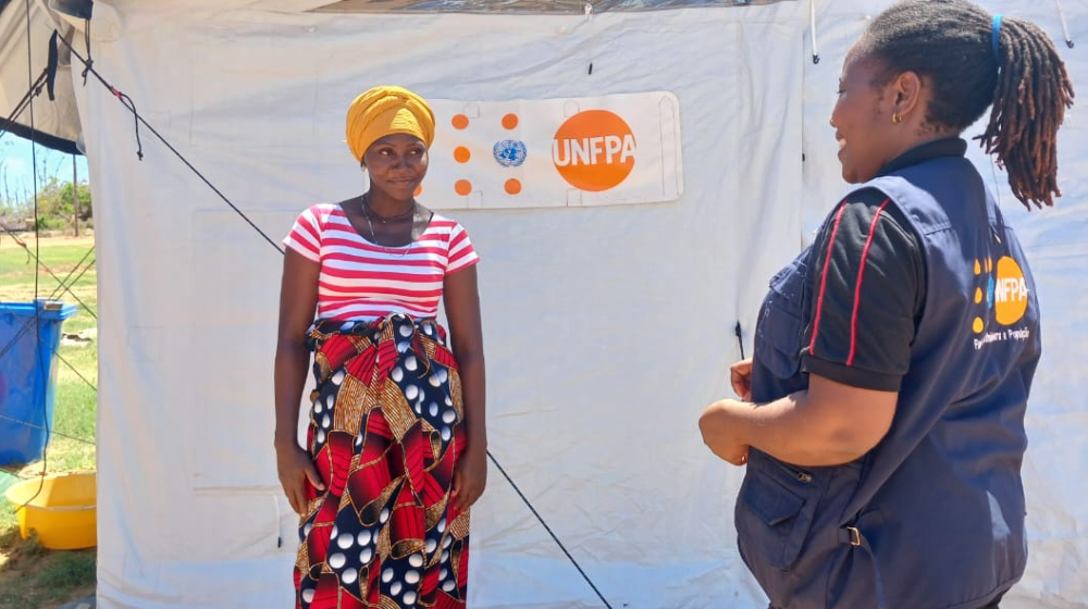 A pregnant woman smiles at a woman in a UNFPA vest outside a tent