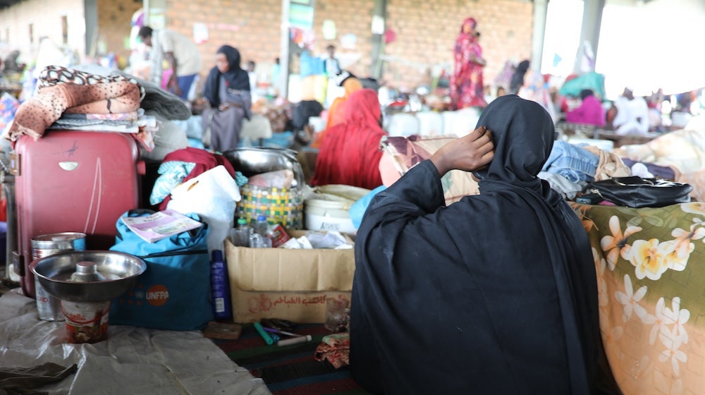 A woman in black sitting with her back turned in a crowded shelter. 