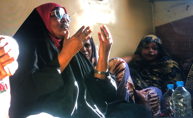 A woman speaks to a group of women, raising her hands