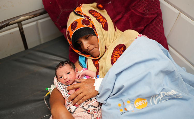 A mother holds her newborn, both laying on a bed