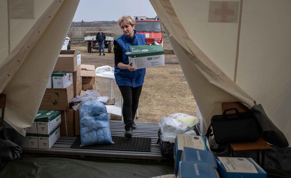 A worker carries aids supplies into a tent.