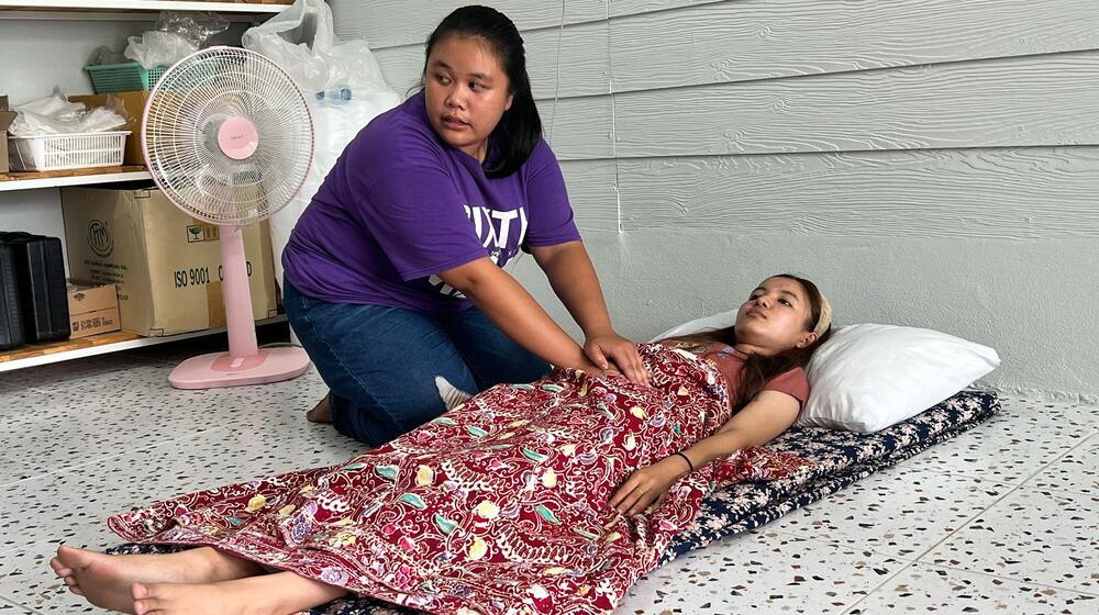 A woman performs a massage on the stomach of a young pregnant woman as is she lays down.