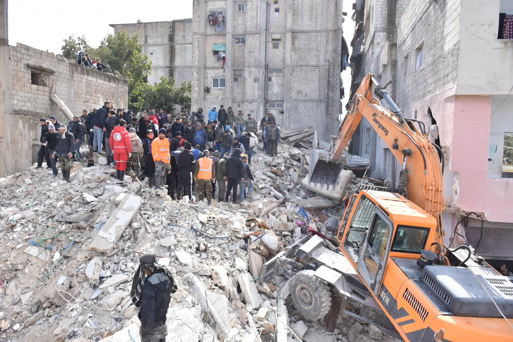 A large group of people stand on top of a collapsed building. 