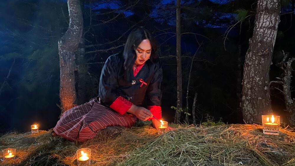 Une femme transgenre allume une bougie devant des arbres, de nuit.