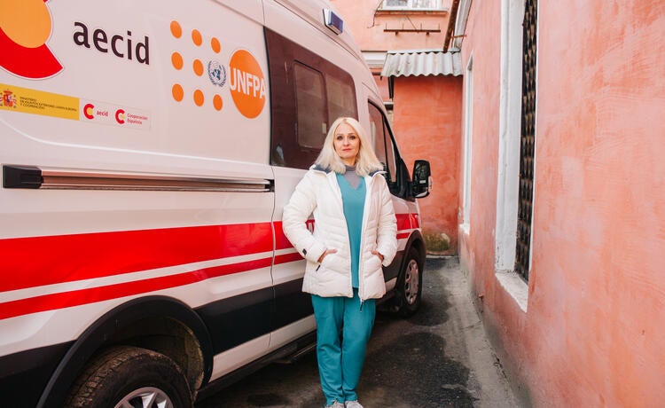 Una mujer delante de una ambulancia con los logotipos del UNFPA y la AECID]