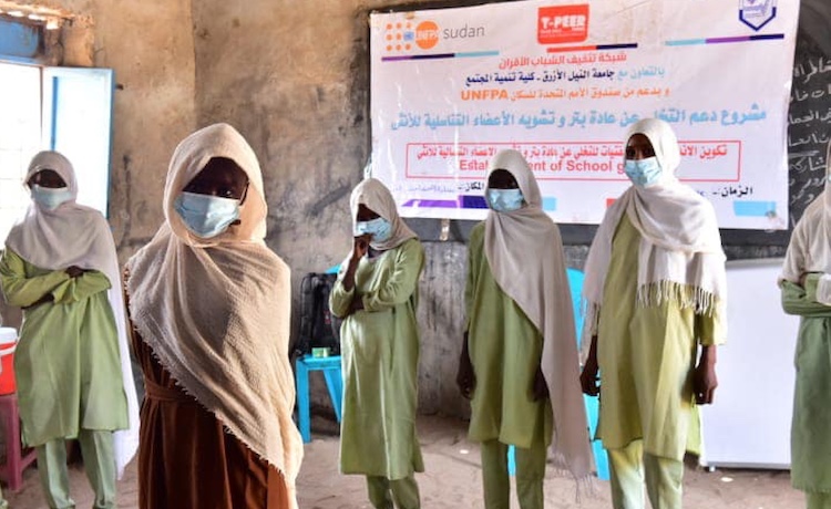 A group of young girls in a classroom stand together. 