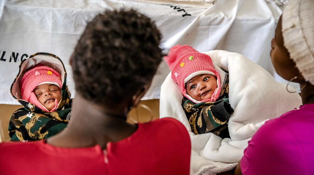 Two babies are held by their mothers.