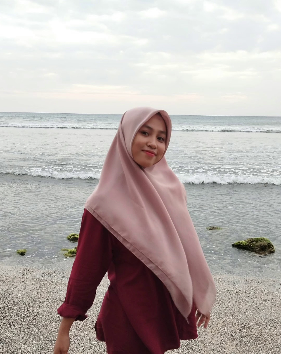 A young woman poses for a photo by the sea.