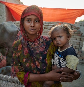 A young women from Pakistan is holding her younger sibling in her arms, gently smiling. 