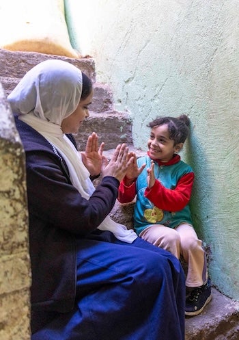 A woman and a young child from Egypt smile as they play a hand-clapping game.