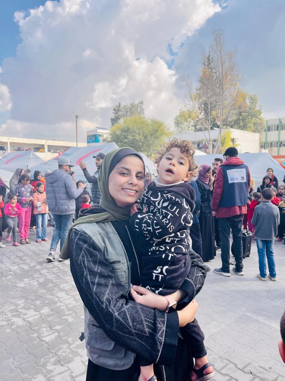 Une jeune femme porte un enfant dans ses bras devant des tentes