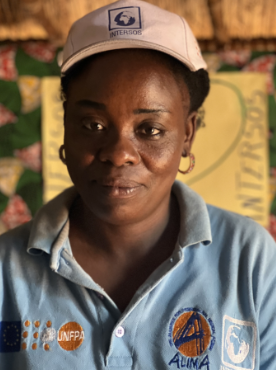 A woman in a blue shirt with UNFPA logo and an INTERSOS cap looks into the camera]