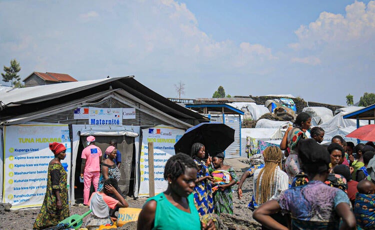 Women gather outside in the sun beside a maternity tent