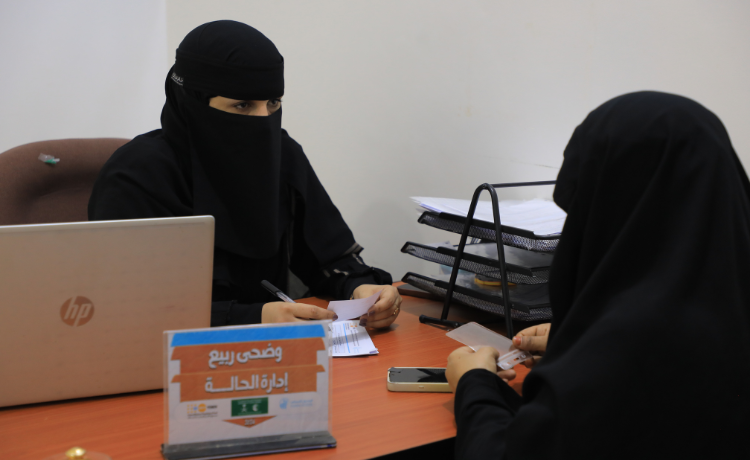 Deux femmes en niqabs noirs assises de chaque côté d’un bureau, sur lequel sont posés un ordinateur portable et un plateau classeur.