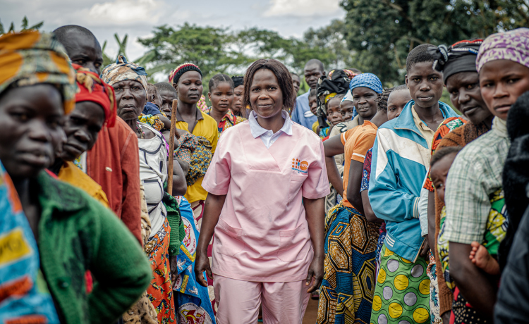 Une agente de santé en uniforme rose se tient debout à l’extérieur, entourée d’autres femmes