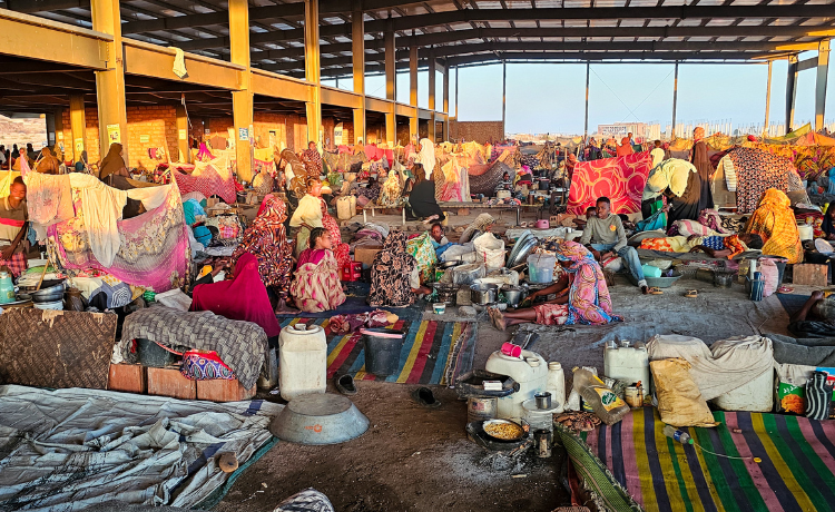 Vue d’un refuge de fortune à ciel semi-ouvert, avec de nombreuses personnes, des tentes, des couchages et des affaires personnelles