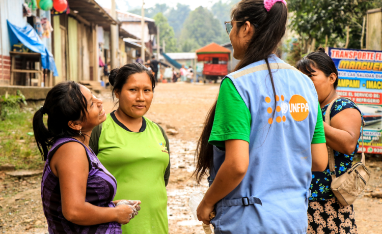 Quatre femmes discutent en cercle. L’une d’elles porte une veste bleue de l’UNFPA. Elles se tiennent toutes dans une rue du village.