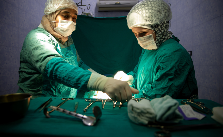  Two health workers in green surgical scrubs, masks and gloves stand beside a table with tools on it