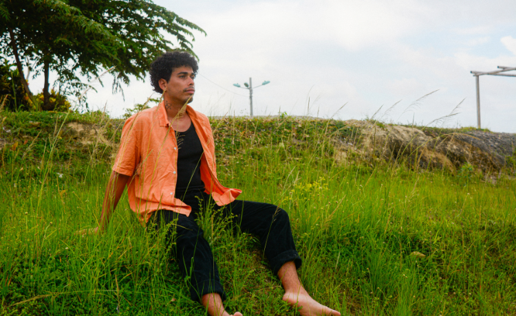 Un homme pieds nus portant une chemise orange est assis sur une colline verdoyante