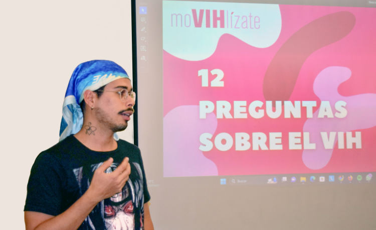 Un joven con gafas junto a una presentación de PowerPoint en una gran pantalla de proyector