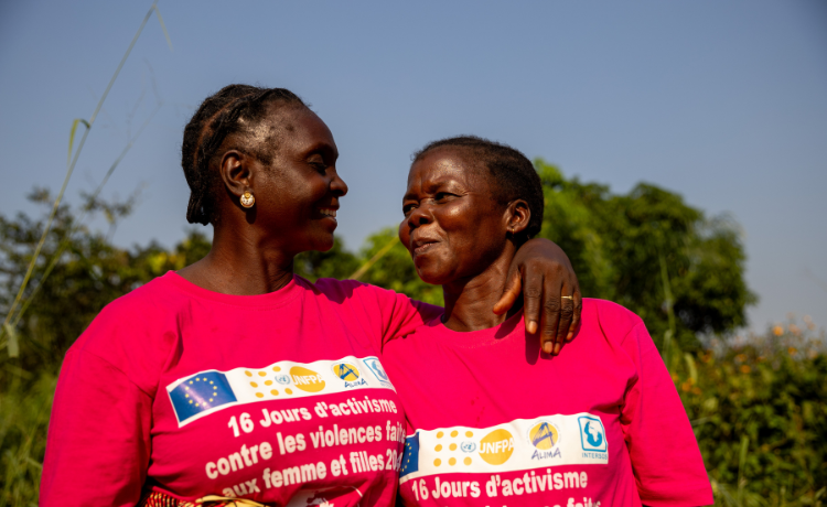 Two women in pink t-shirts embrace and smile at each other