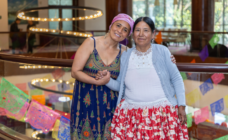 two women wearing colourful clothes hold hands and look at the camera smiling