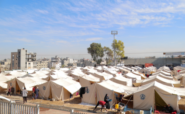 Vue d’une multitude de tentes blanches ; on voit des personnes déplacées au premier plan