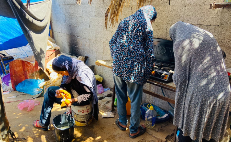 Three girls work cooking and cleaning beside an open tent]