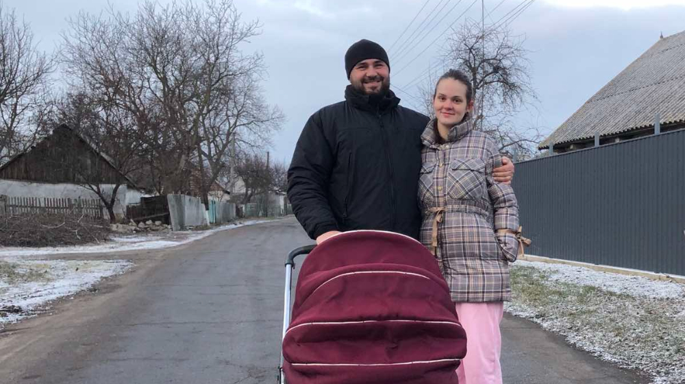 A couple smile with their newborn child who is in a pushchair.