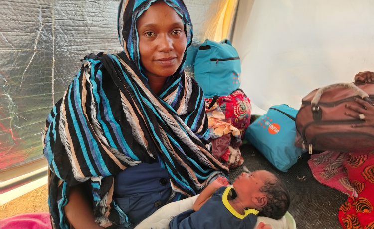  A woman dressed in blue and black stripes holds a newborn baby.