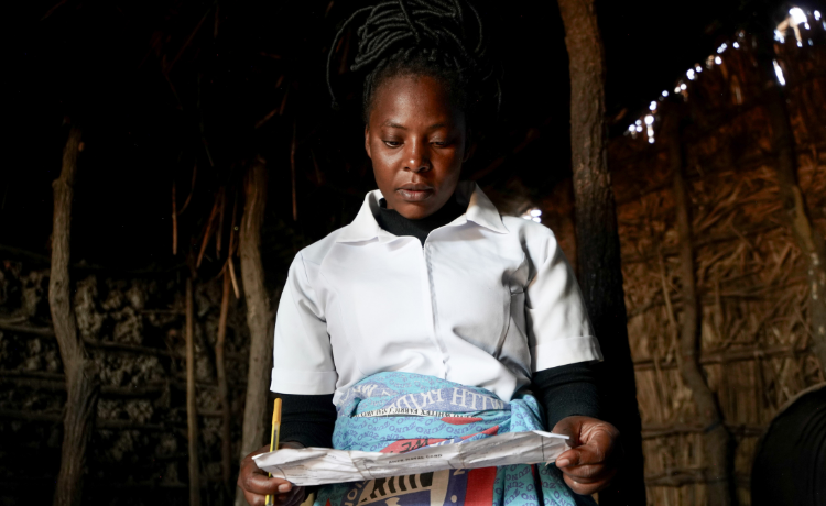 A nurse looks down at a sheet of paper, holding a pen in her right hand.