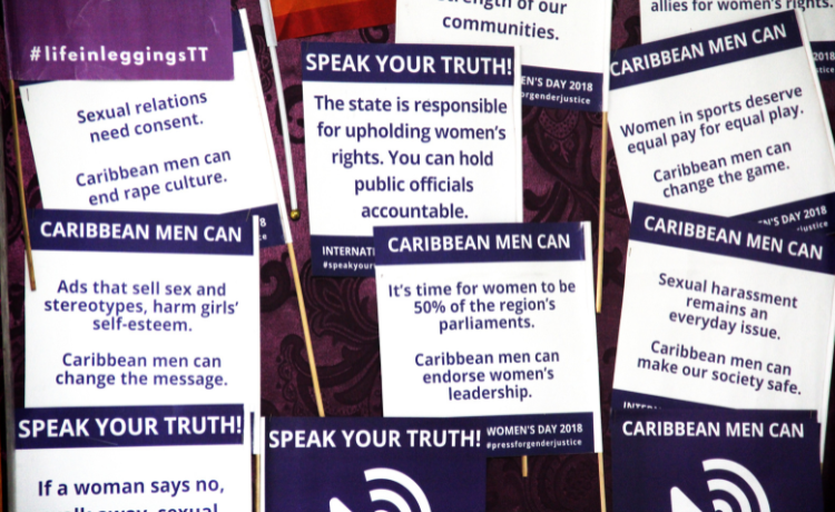 Purple and white placards say “Caribbean men can” and “Speak your truth”, encouraging people to support gender equality.