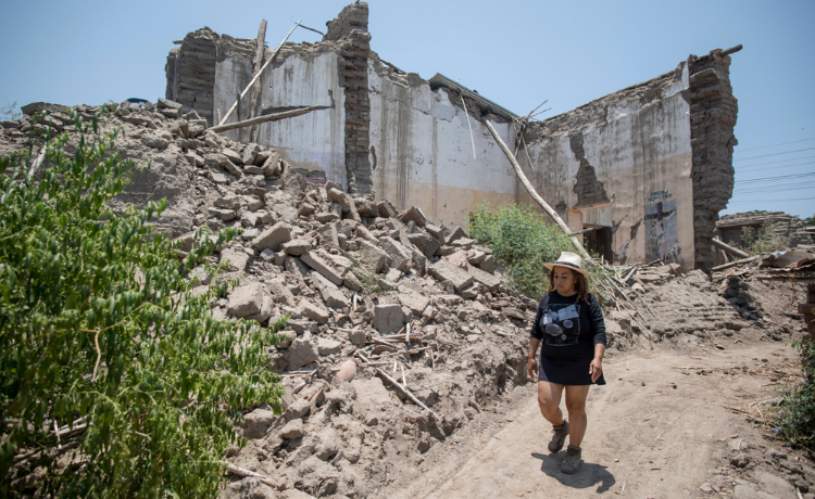 Una mujer avanza por un camino de tierra junto a un edificio destruido.