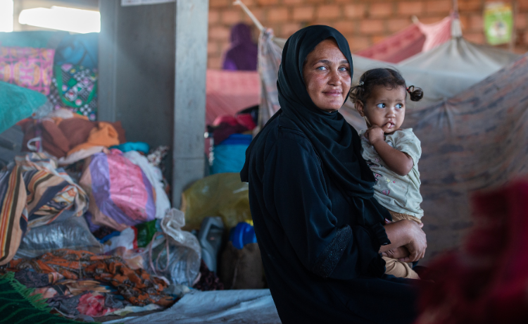 A woman dressed in black holding a young girl is surrounded by tents and luggage.