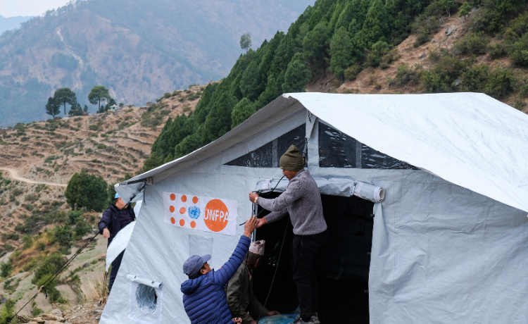 Un homme portant un pull de l’UNFPA aide à installer une tente qui servira de clinique mobile