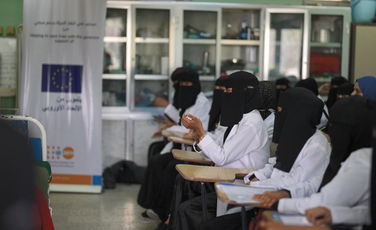 Un grupo de mujeres con ropa médica en pupitres mira hacia el frente de la clase