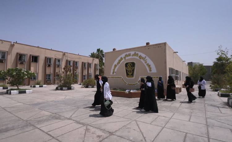 Un grupo de mujeres atraviesa un patio frente al gran edificio de una institución educativa