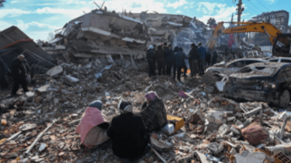 Three women sit together on top of rubble. 