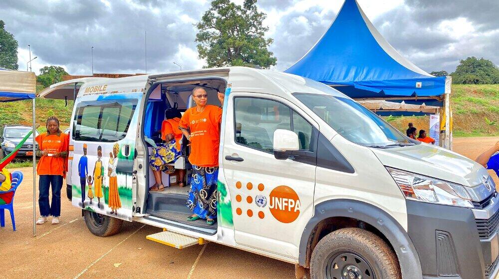 Woman in orange shirt stands in door entry of a UNFPA van.