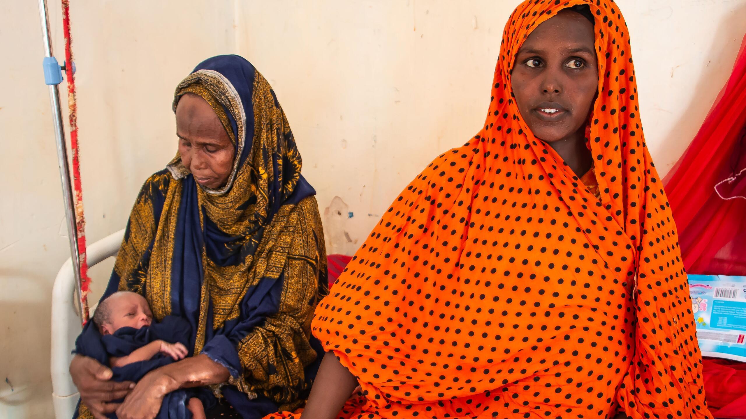 Two women sit with a newborn child.