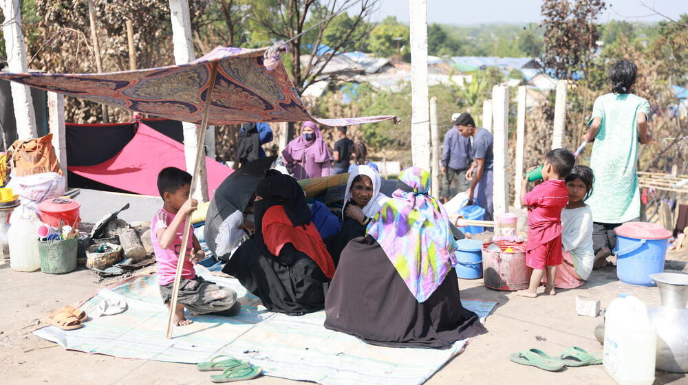 A group of Rohingya refugees who are homeless again after a fire broke out in their camp are seated on a mat on the ground.  