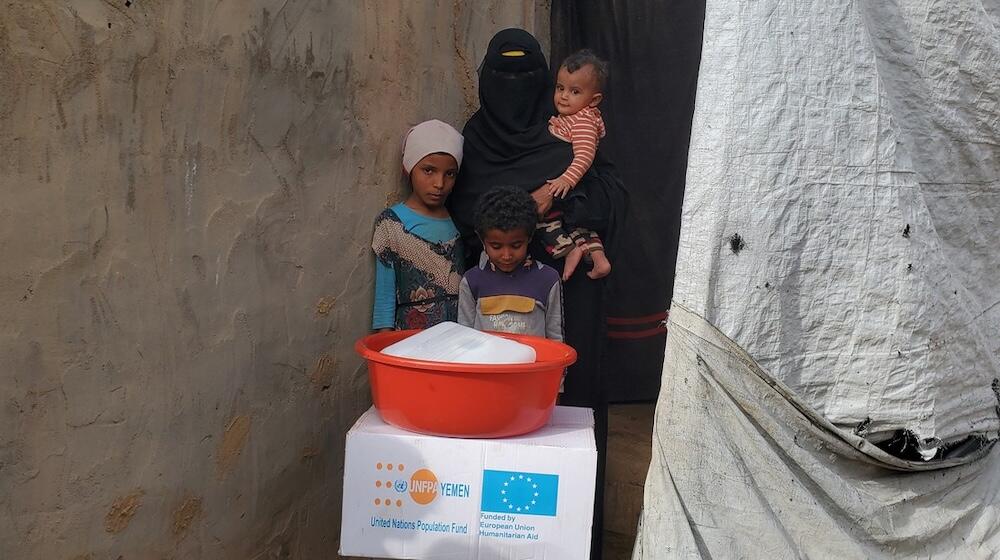 A woman stands with three children in front of a box and a basin.