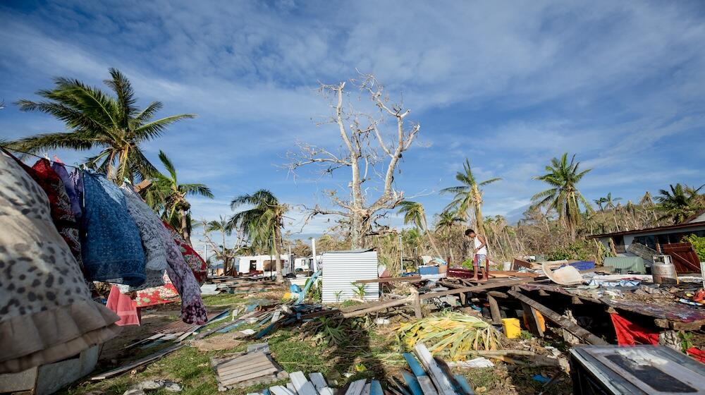 Un homme se tient au milieu de bâtiments en ruines, de débris d’arbres et d’eau.