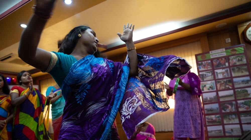 Un grupo de personas transgénero y de género diverso visten ropa colorida bailan y aplauden.