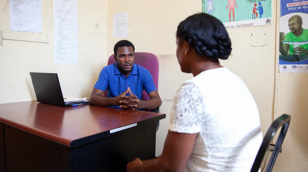 A man speaks with a woman across a desk