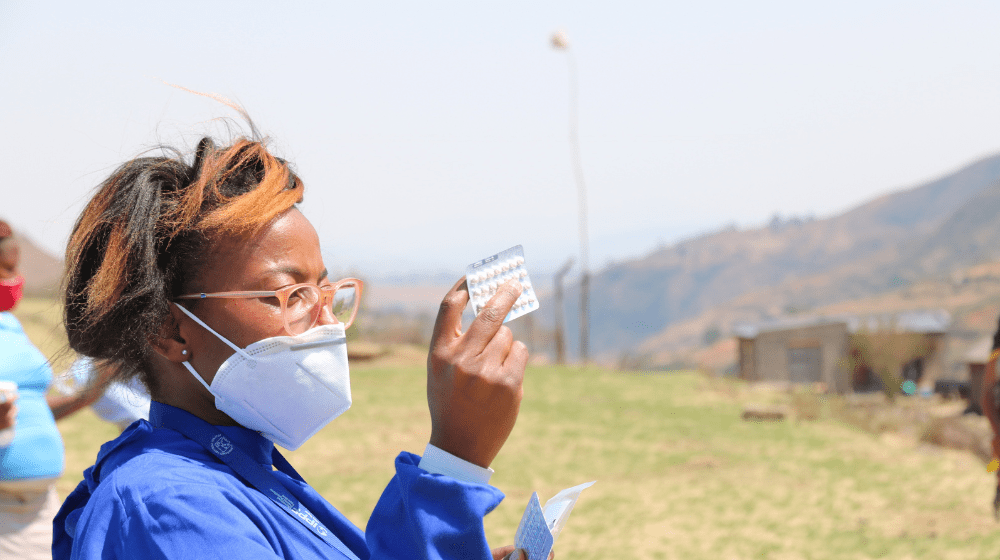 A woman holds a pack of pills.