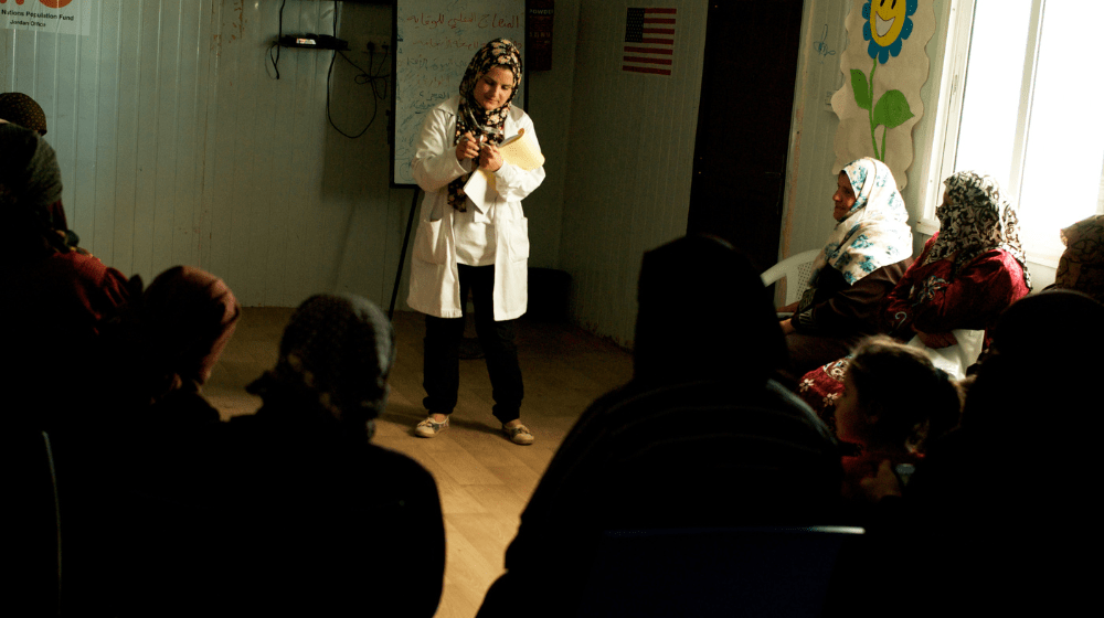 A health educator stands in front of a crowd of women over 35 providing information on menopause and breast exams.